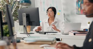 Asya 'lı güzel gözlüklü, zarif bir kadın kulaklık takmış, kulaklık takmış bir şirkette oturuyor. Bilgisayarın önünde müşterilerine danışmanlık yapıyor..