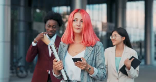 Irodai asszisztens a főnök kisétál a munkatársak üzleti találkozóra üveg épület cég nő rózsaszín haja öltözött kockás kabát hordozza dokumentumok hónalj alatt olvasott üzenetek telefonon — Stock videók