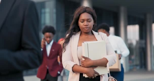 Una bella donna afroamericana dalla carnagione scura esce dall'ufficio aziendale con dei colleghi, la ragazza tiene in mano una cartella di documenti, la segretaria vestita con abiti eleganti — Video Stock