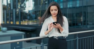 Şirkette çalışan güzel, güler yüzlü bir kadın ara vermek için dışarı çıkıyor şık kıyafetler içinde cam binanın önündeki parmaklıklara yaslanıp elinde telefonla kahkahalar atarak haberleri okuyor.