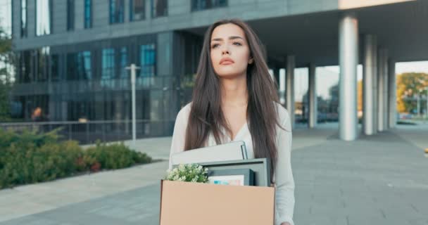 Mujer camina delante de vidrio moderno edificio de oficinas de la corporación donde trabajó siendo despedido de su posición chica con triste mirada incierta en la cara de la caja de espera de pertenencias empacadas desempleo — Vídeo de stock