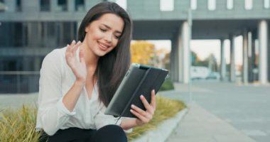 Beyaz gömlekli güzel, hırslı iş kadını cam önünde oturuyor. Sigorta şirketinin modern binasının önünde. Kadın tableti elinde tutuyor.