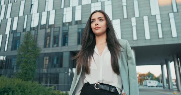 Secretaria de mujer de negocios sonriente en maquillaje diurno mujer en camisa blanca con chaqueta arrojada por la noche fría de la mañana afuera frente al edificio de oficinas corporativas de vidrio cruza brazos en el pecho — Vídeos de Stock