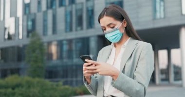 Ofis çalışanı, sekreter, gömlek ve ceket giymiş, yüzünde koruyucu maske olan iş kadını şirket binası önünde duruyor, işten çıkıyor, telefonla mesajlar yazıyor.