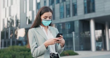 Ofis çalışanı, sekreter, gömlek ve ceket giymiş, yüzünde koruyucu maske olan iş kadını şirket binası önünde duruyor, işten çıkıyor, telefonla mesajlar yazıyor.