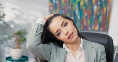 Cilveli, seksi, koyu renk gözlü esmer, zarif giyimli iş kadını şirket sekreterinin ofisinde oturmuş kameraya gülümseyen, saçlarıyla oynayan, parmaklarıyla tarayan.