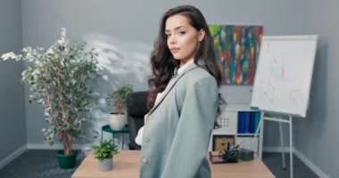 Kahverengi saçlı güzel bir kız şirket binasında duruyor. Arkaya atılmış şık bir gömlek giymiş, kollarını göğsüne kavuşturarak odadan çıkmaya hazırlanıyor.