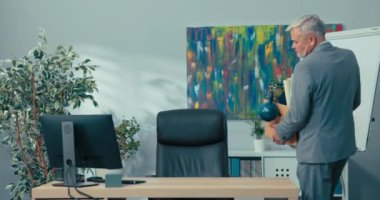 Tişört giymiş deneyimli bir adam şirket ofisindeki masanın önünde duruyor. Elinde paketlenmiş eşyalar olan bir kutu şirkete terfi etmek için geliyor. Koltuğa oturuyor.