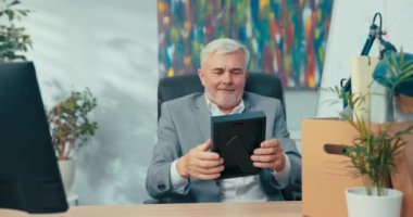 Tişört giyen hırslı yaşlı adamlar şirket ofisindeki masanın önünde oturmuş paketlenmiş eşyaları tutuyorlar şirkete yeni bir işe terfi ettirmek için aksesuarları açıyorlar.