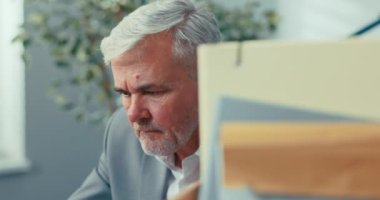 Çalışanların eşyalarıyla birlikte karton kutunun arkasından çekilen, iş yerindeki ekipman belgeleri, yoğunlaşmış gri saçlı yaşlı adam dizüstü bilgisayar raporlarına bakıyor ve e-postaları okuyor.