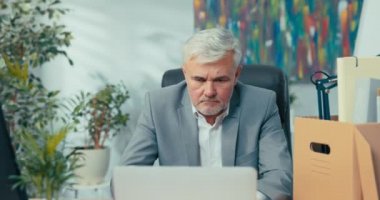 Beyaz gömlekli, gri saçlı, sakallı, gülümseyen bir adamın yakın plan fotoğrafı. Şirketin rahat koltuğunda oturuyor. Kameraya dost canlısı patron, neşeli müdür.