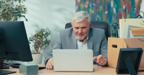 Άνδρας με κοστούμι με γκρίζα μαλλιά οδηγεί απομακρυσμένη συνομιλία από το γραφείο, κάθεται στο γραφείο μπροστά από την οθόνη του φορητού υπολογιστή, χαιρετώντας τους συναδέλφους σε απευθείας σύνδεση συναντήσεις μέσω webcam συνομιλία βίντεο μιλάει για εντυπώσεις — Αρχείο Βίντεο