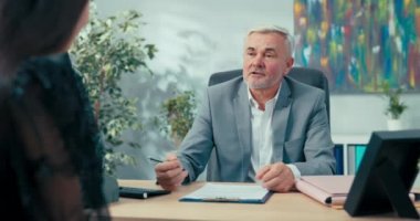 Karşısındaki masada oturan yaşlı patronla iş görüşmesi. Sekreterlik pozisyonu için başvuran kadın. Kız kıza sorular soruyor.