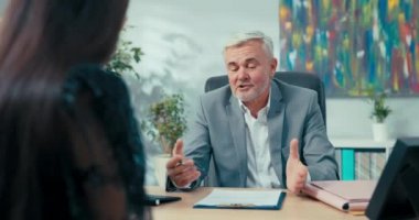 Karşısındaki masada oturan yaşlı patronla iş görüşmesi. Sekreterlik pozisyonu için başvuran kadın. Kız kıza sorular soruyor.