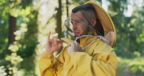 A beekeeper gets ready for work in the forest at the apiary with bees, hives, he puts on a hat with a protective net, a mosquito net on his head to protect him from insect bites — Stock Video