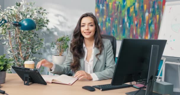 Klasik makyajlı çekici esmer, gömlek giyiyor bilgisayar başında şirket önünde masada oturuyor. Programı kontrol eden sekreter toplantılara önemli bilgilerle katılıyor. — Stok video