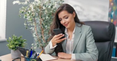 Sosyal medya, pazarlama ve müşteri iletişimi uzmanı şirket ofisinde telefon başında oturur, satış ilanları, reklamlar ekler, kameraya telefon tebessümleri koyar.