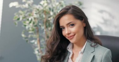 Flörtöz, güzel, oldukça seksi, koyu renk gözlü esmer, zarif giyimli kadın, iş kadını şirketin ofisinde oturuyor, sekreter, asistan, kameraya göz kırpıyor.