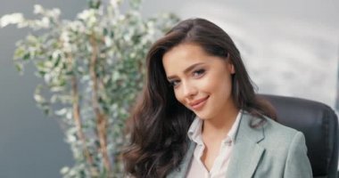 Flörtöz, güzel, oldukça seksi, koyu renk gözlü esmer, zarif giyimli kadın, iş kadını şirketin ofisinde oturuyor, sekreter, asistan, kameraya göz kırpıyor.