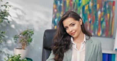 Gülümseyen, güzel, seksi, koyu renk gözlü esmer, zarif giyimli, iş kadını şirket ofisinde oturuyor, sekreter, asistan, kameraya göz kırpıyor, büyük boyalı dudaklar.