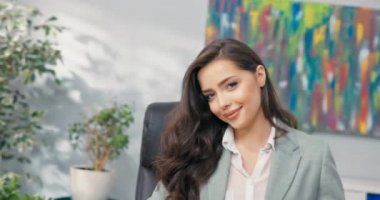 Gülümseyen, güzel, seksi, koyu renk gözlü esmer, zarif giyimli, iş kadını şirket ofisinde oturuyor, sekreter, asistan, kameraya göz kırpıyor, büyük boyalı dudaklar.