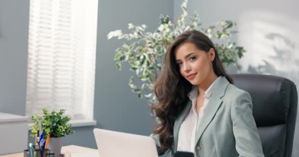 Trabalhador de escritório corporativo atraente senta-se na mesa na frente da tela do laptop olha para a câmera encantadoramente sorrindo flertando bela secretária gerente de cabeça corporativa com olhos de cabelo marrom bonita — Vídeo de Stock