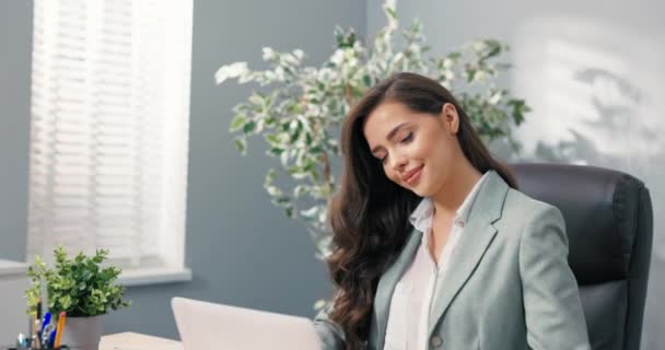 Attraktive Büroangestellte sitzt am Schreibtisch vor dem Laptop-Bildschirm blickt charmant lächelnd kokett schöne Sekretärin Konzernchef Manager mit hübschen braunen Haaren Augen — Stockvideo