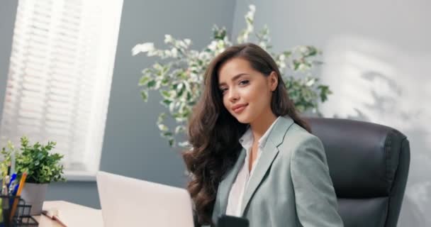 Trabalhador de escritório corporativo atraente senta-se na mesa na frente da tela do laptop olha para a câmera encantadoramente sorrindo flertando bela secretária gerente de cabeça corporativa com olhos de cabelo marrom bonita — Vídeo de Stock