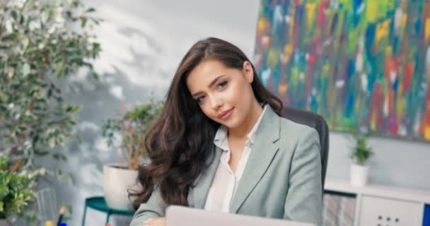 Närbild skott av attraktiva företagskontor anställd sitter vid skrivbordet ser in i kameran charmiga leende flirtig vacker företagssekreterare chef chef med fina bruna hår ögon — Stockvideo