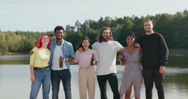 Porträt von sechs Freunden, die sich am Strand am See amüsieren, locker gekleidet den Abend verbringen, das Treffen feiern, Bier aus Glasflaschen trinken, Studentengruppe — Stockvideo