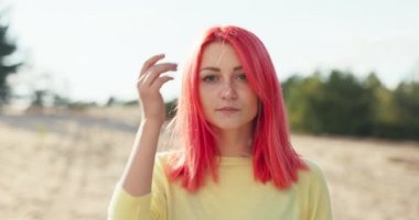 Yüzü güzel, pembe saçlı, rüzgarda savrulan, kulağının arkasına çektiği güzel bir kız. Yüzünde çiller, uzun, kalın kirpikleri olan bir kadın sahilde ağaçların arasında duruyor.