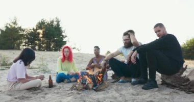 Çalışmaktan yoruldular, öğrenciler plajda şenlik ateşinin başında dinleniyorlar, cam şişelerden bira içiyorlar, konuşuyorlar, gitar tutan bir kadın müziği hoş hale getiriyor.
