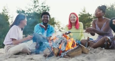 Sosyalleşen öğrenciler kamp ateşinde birbirlerini tanırlar, farklı ten renkleri, milletler, konuşurlar, şakalaşırlar, gülerler, ateşin yanında kumda otururlar, çubuklarda sosis kızartırlar, bira içerler.