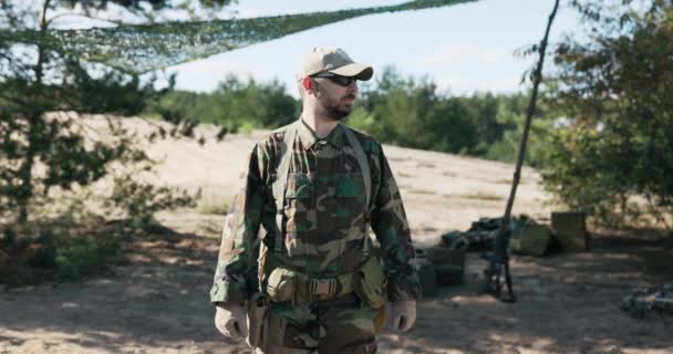 Asker, asker, bölge savunma ekibi üyesi, moro kıyafetler giymiş, siyah gözlükler arka planda duruyor, kamp, kollarını göğsünde kavuşturuyor, kendinden emin, cesur. — Stok video