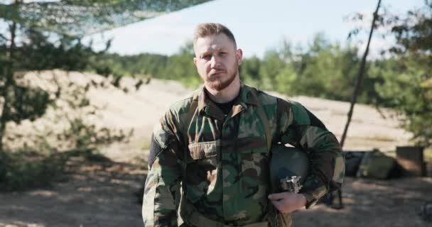 Un soldado cansado, un militar, un hombre del equipo de defensa territorial, vestido con ropa moro, sosteniendo un casco bajo el brazo, mira a la cámara con una cara seria y triste — Vídeo de stock