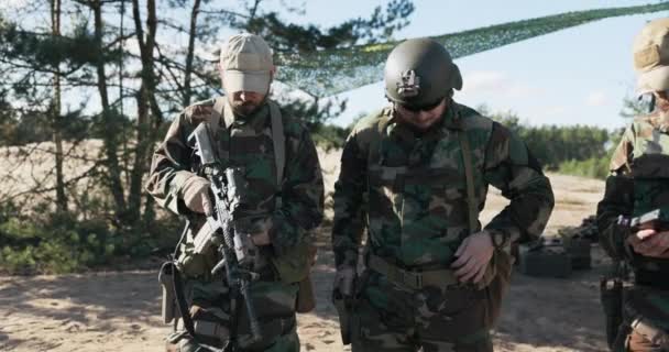 4人の男性は、彼らは武器をチェックし、武器をチェックし、短いピストル、長いライフルをロックし、ベルトのポケットに隠れて、モロの制服を着た警備員、領土を守るために準備中の軍隊に立っている — ストック動画