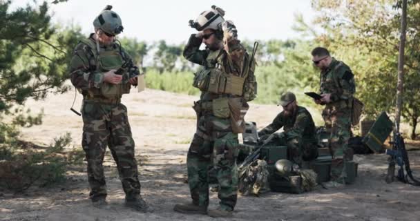 Un grupo de soldados se prepara para patrullar en el campo, establecen una estrategia, una ubicación, siguen un mapa en una computadora, una tableta, un líder de tropas se pone un casco — Vídeos de Stock