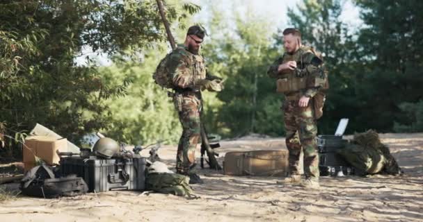 Dwóch żołnierzy przygotowuje się do ćwiczeń terenowych, odpowiedzialnej pracy, obrony terytorialnej, wojska na misji, mundurów moro, ciężkich plecaków, amunicji i pasów uzbrojenia, bazy w bushe — Wideo stockowe