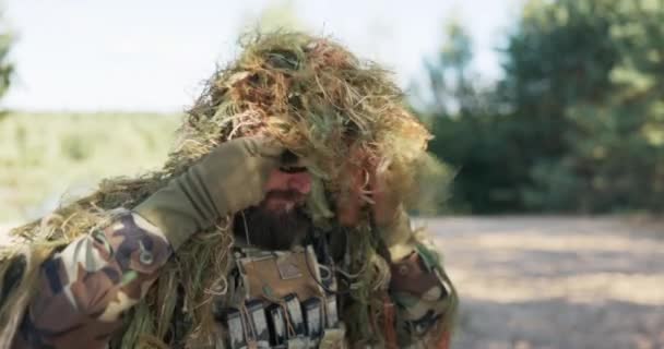 Homme à barbe commandant militaire de l'armée, vêtu d'uniforme porte un manteau de camouflage fait de mousse, sur les yeux des lunettes noires, prêt pour des missions, des actions, des exercices, un soldat défendant le territoire — Video