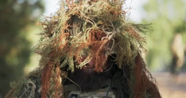 Homme hors territoire de défense portrait de soldat courageux lève la tête en regardant dans la caméra à travers des lunettes noires par la bouche microphone caché de casque camouflage de mousse de gazon artificiel — Video