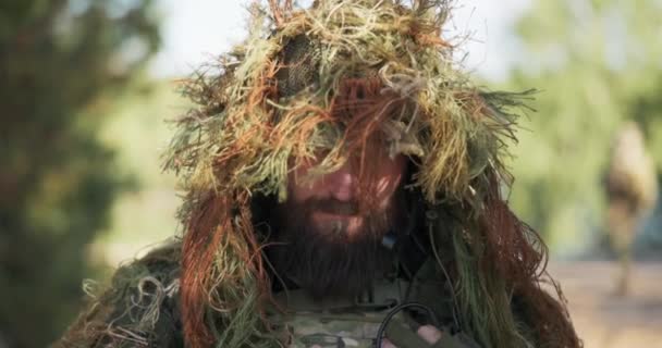 外の男は領土、勇敢な兵士の肖像画を守る、人工芝、苔の頭のカモフラージュで、ヘッドフォンから隠された口のマイクでカメラに頭を上げる — ストック動画
