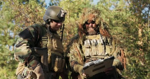 Δύο στρατιώτες έτοιμοι για δράση, ντυμένοι με στολή, καμουφλάζ συζητούν στρατηγική, τοπογραφία του εδάφους κοιτάζοντας το θωρακισμένο λάπτοπ, μιλώντας για λεπτομέρειες της αποστολής. — Αρχείο Βίντεο