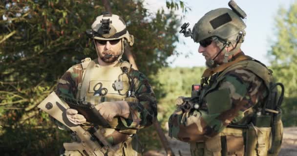 Het leger bereidt zich voor op een oefening, mannen gekleed in moro uniformen met geweren over hun schouders, helmen op hun hoofd, controleer details van de actie op een tablet, neem contact op met de legerbasis — Stockvideo