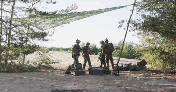 Soldaten trekken het veld in vanaf de militaire basis waar ze kisten met uitrusting achterlaten, op zoek naar de vijand, gekleed in uniformen, met lange wapens op hun schouders, voeren missies uit, acties — Stockvideo