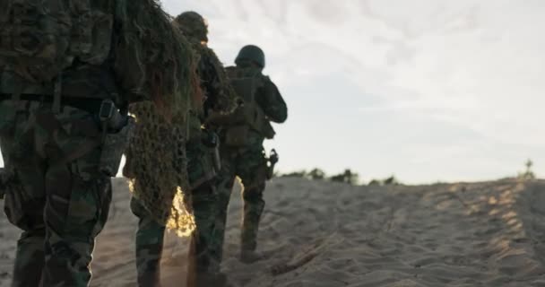 군인들은 모래 위에서 행진하고, 야전 훈련, 훈련 장소, 감시 구역, 순찰하고, 위장 위장, 구울, 풀, 배낭, 헬멧, 손에 들고 있는 소총, 군 복무, 경비 — 비디오