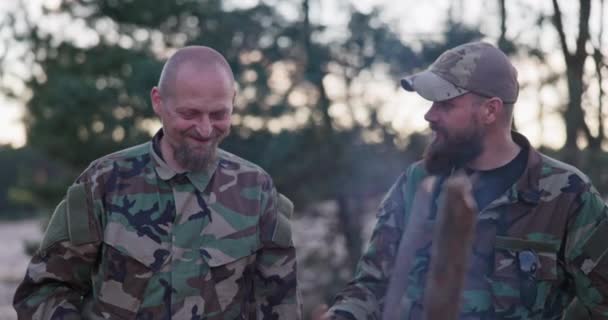 Soldats vêtus de vêtements de camouflage, discutant le soir à un feu de joie commun saucisses à frire pour le souper, hommes plaisantant, riant, se reposant après le travail, service, exercices sur le terrain — Video