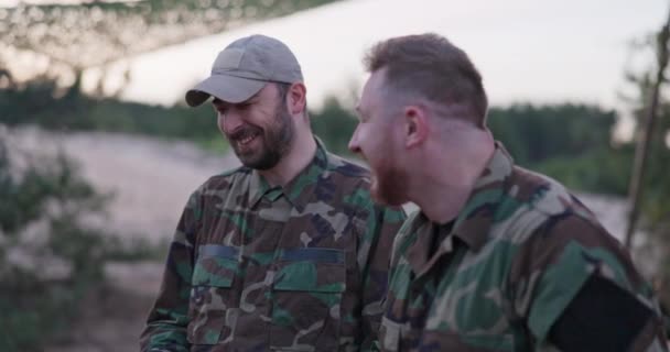 Soldats vêtus de vêtements de camouflage, discutant le soir à un feu de joie commun saucisses à frire pour le souper, hommes plaisantant, riant, se reposant après le travail, service, exercices sur le terrain — Video