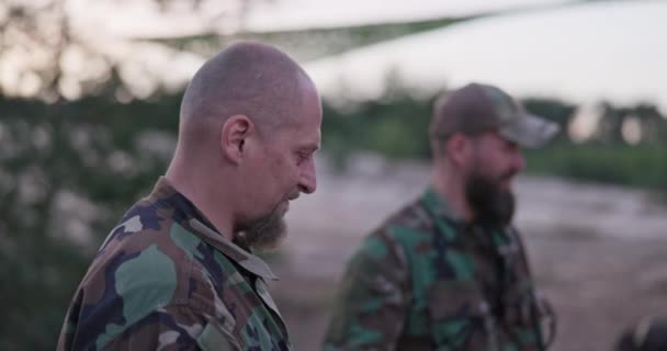 Conversation des soldats en vêtements de camouflage, ils discutent dans la soirée par les saucisses de friture de feu de joie commun pour le souper, les hommes se reposent après le travail, le service, les exercices sur le terrain — Video
