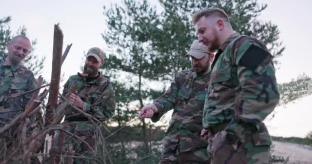 Gesprek van soldaten in camouflage kleding, bespreken ze in de avond door de gemeenschappelijke kampvuur bakken worsten voor het avondeten, mannen rusten na het werk, dienst, veldoefeningen — Stockvideo