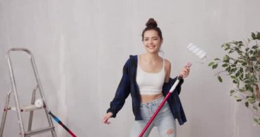 Dar tişört giymiş, gülümseyen güzel bir kız merdivenin yanındaki duvarlarda boya çubuğuyla dans ediyor. Yeni dairesinde son rötuşlar ve yenileme çalışmaları için zaman harcıyor.